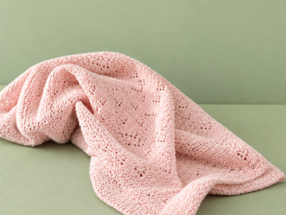 A soft blush-pink knitted baby blanket arranged in gentle folds on a sage-green background.